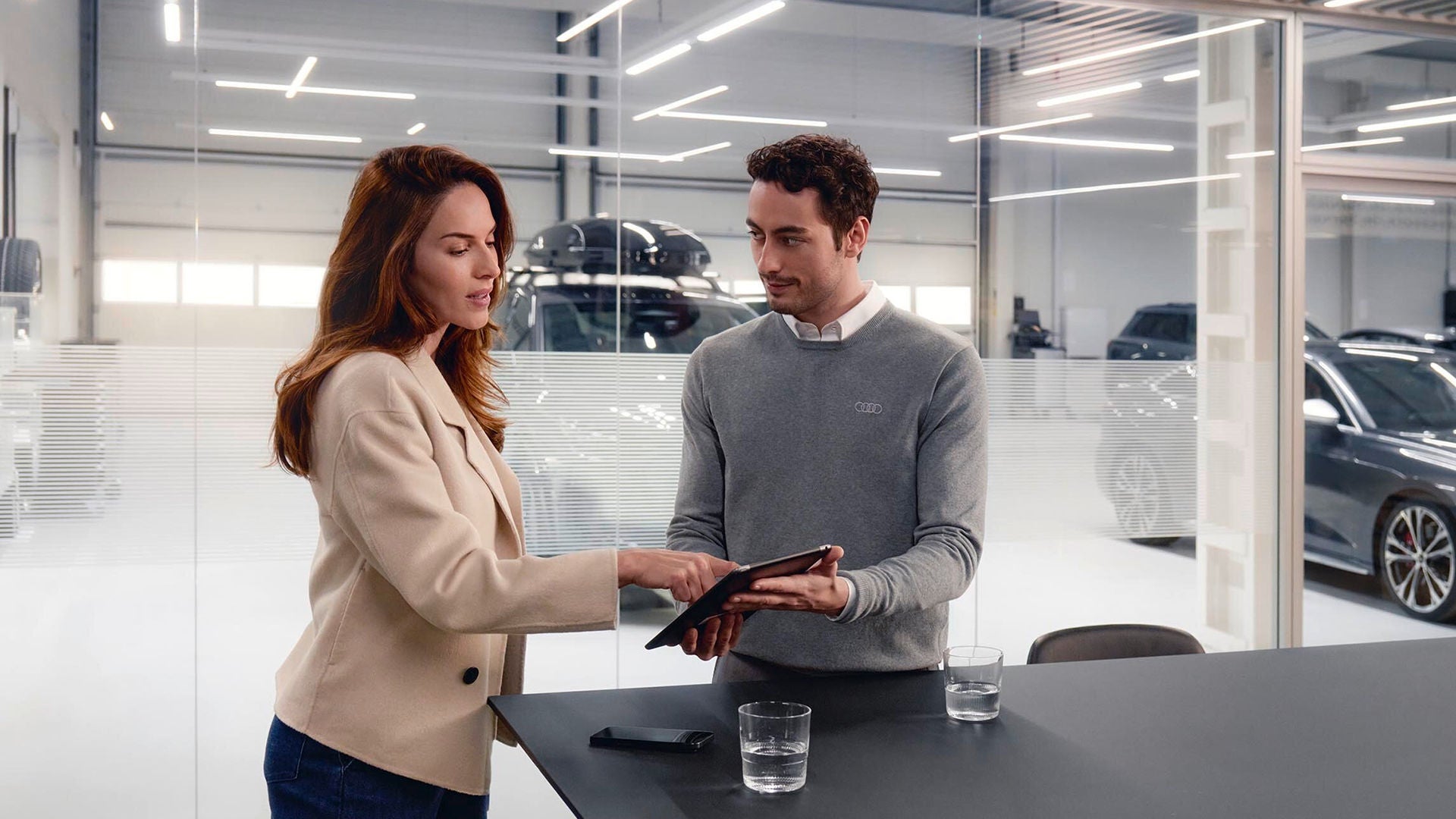 Consulente Audi che mostra a cliente Audi i piani di manutenzione su tablet in concessionaria