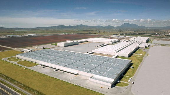 Luftaufnahme des Audi Werks in Mexiko mit großen Hallen, Parkplätzen und umliegender Berglandschaft.