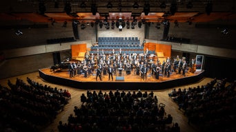 Konzertsaal mit Bühne im Mittelpunkt, auf der die Audi Bläserphilharmonie spielt.
