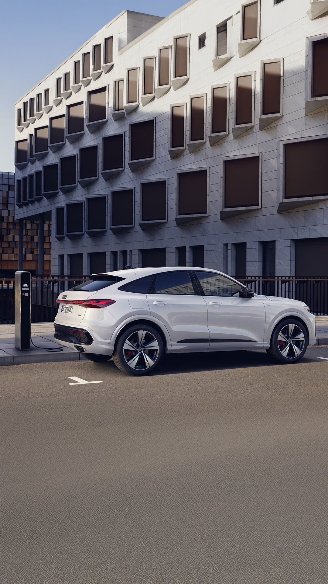 Valge Audi Q5 Sportback e-hybrid külgvaates laadimas tee äärses laadimiskohal