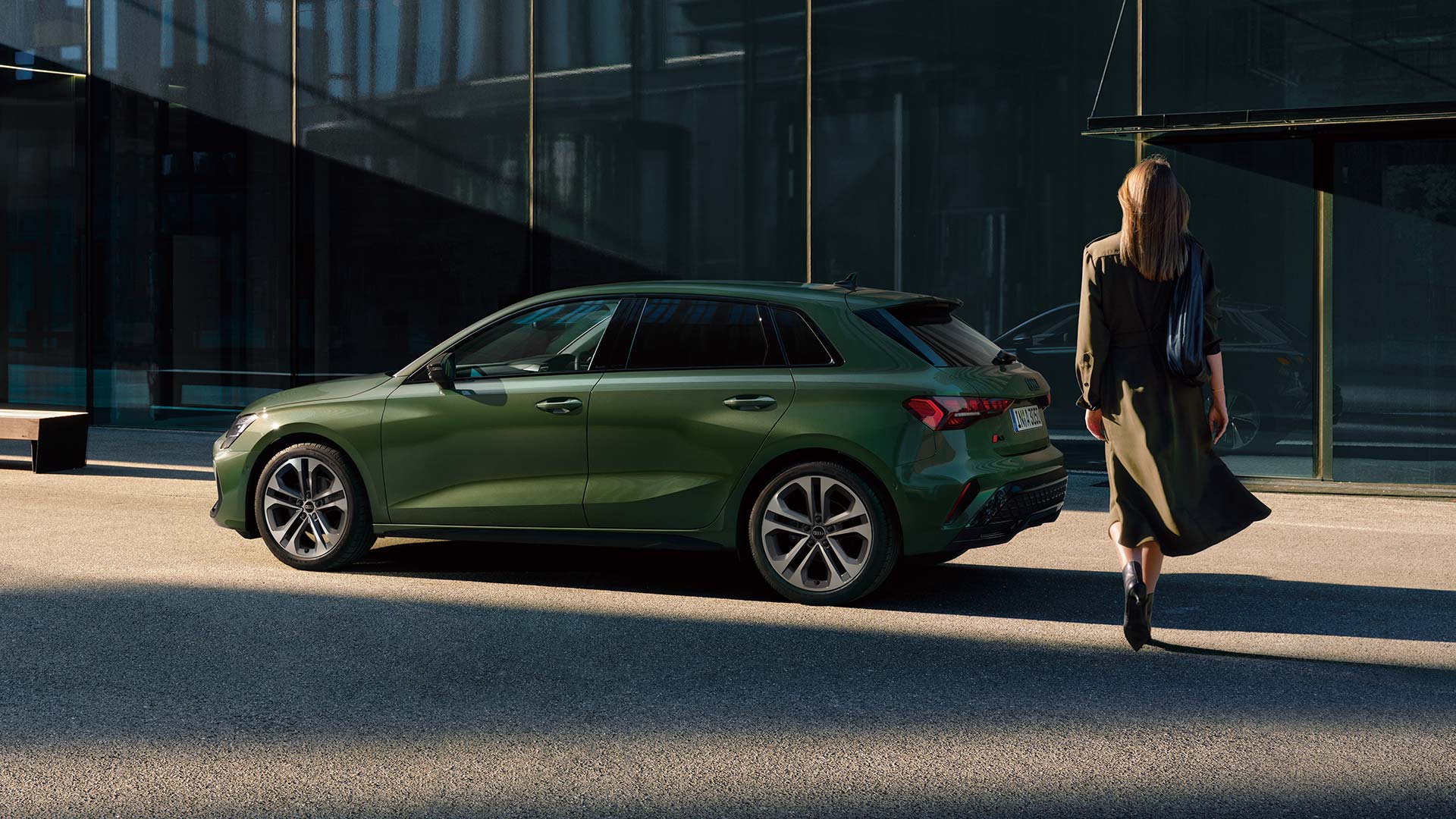緑色のAudi A3 Sportbackの横を歩く女性