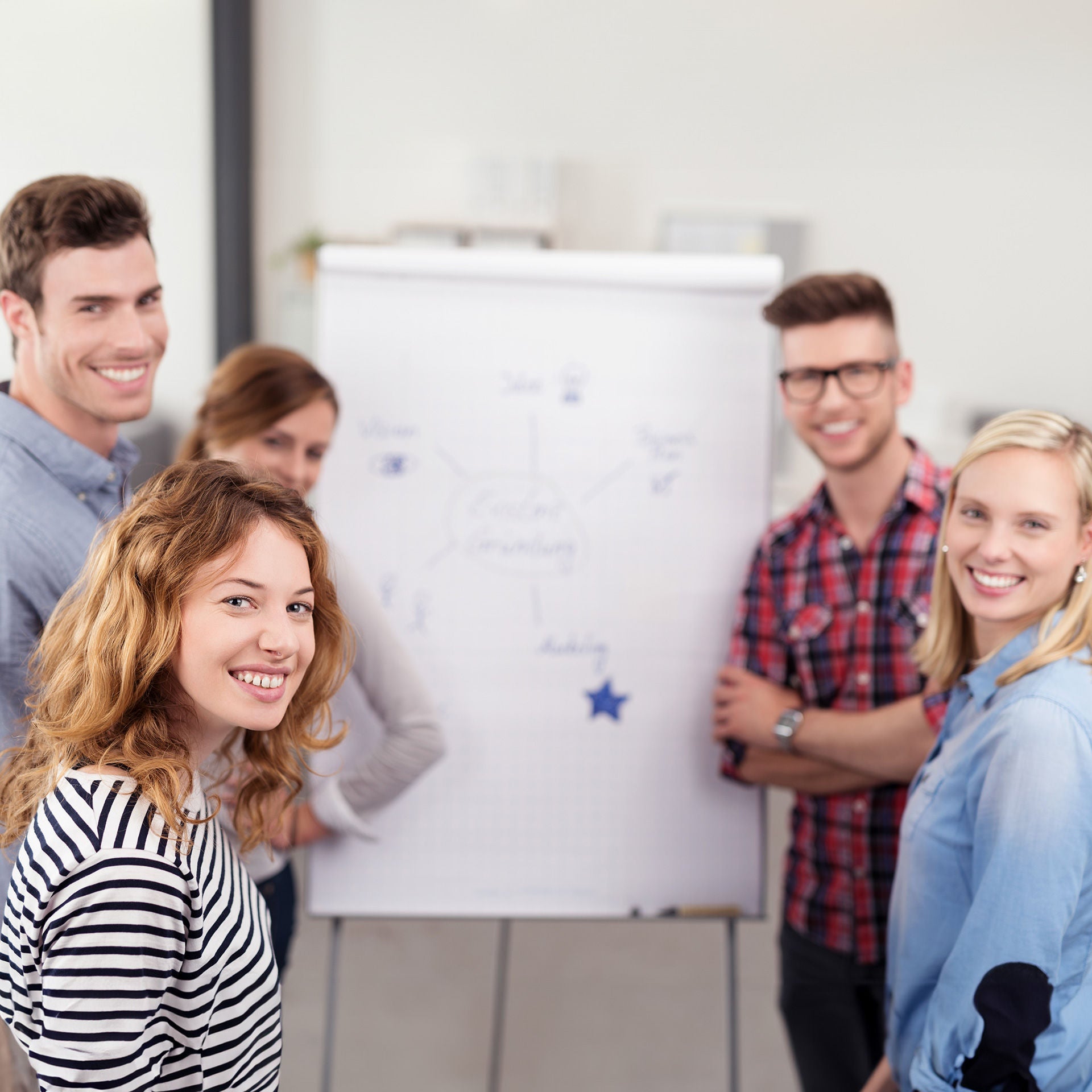 Friendly smiling team in casual outfit grouping in front of a Flipchart smiling
