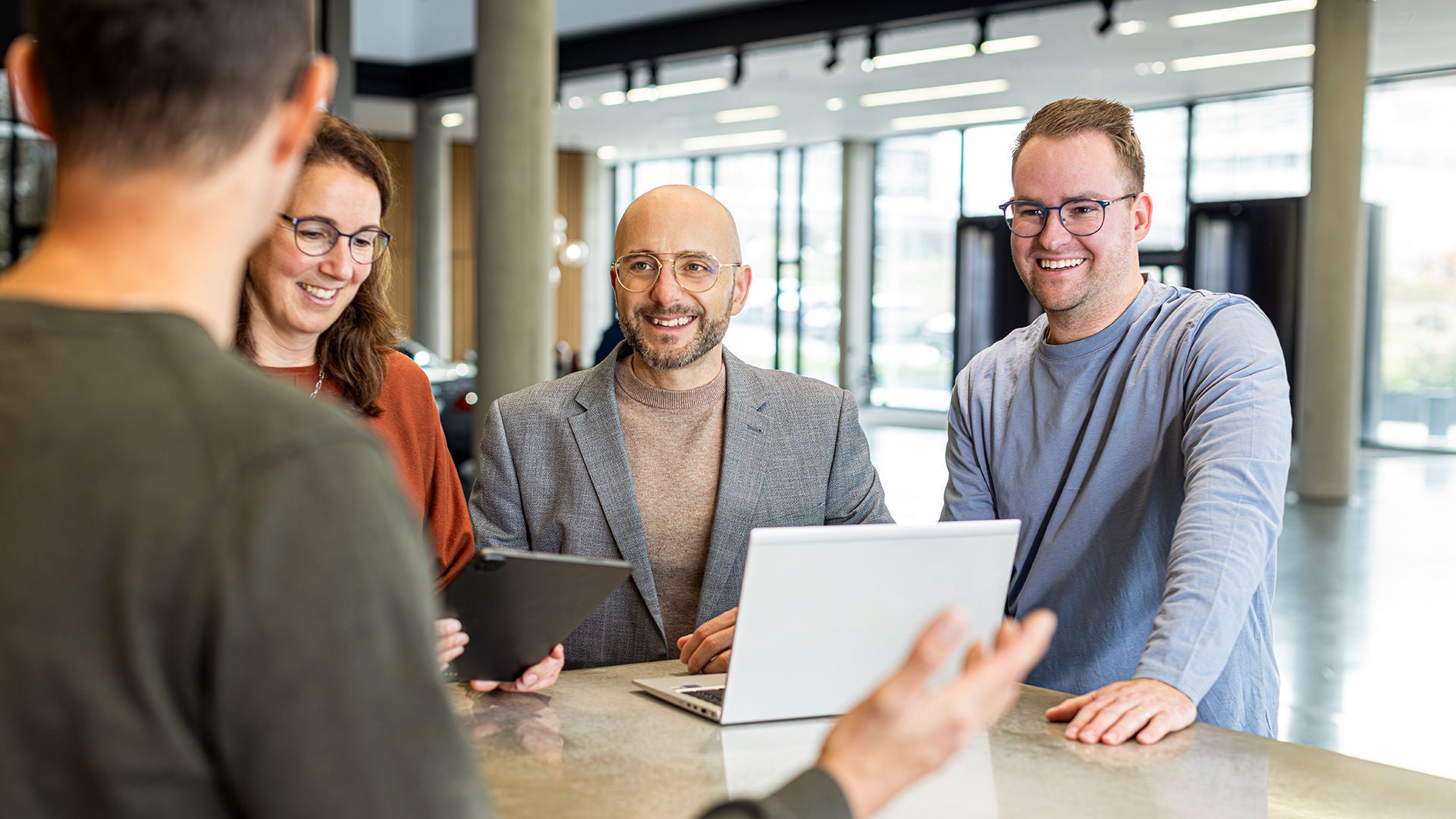 Mario De Felice is standing with colleagues at a table with a laptop on it and laughing