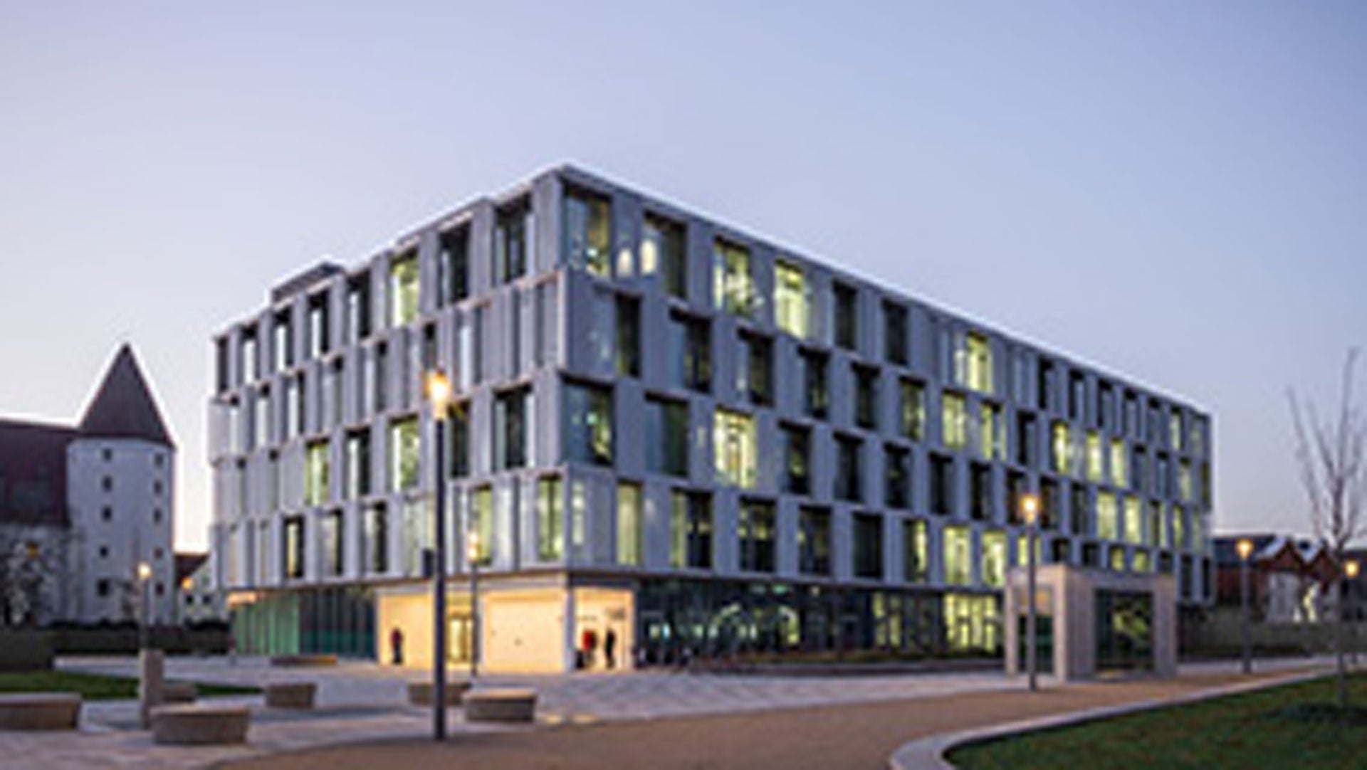 Modernes Bürogebäude mit vielen Fenstern, beleuchtet bei einsetzender Dunkelheit.