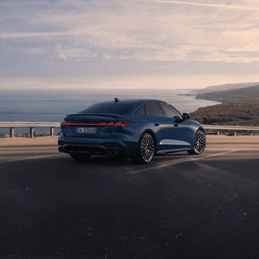 Blue sedan on coastal road at dusk with ocean horizon in background.