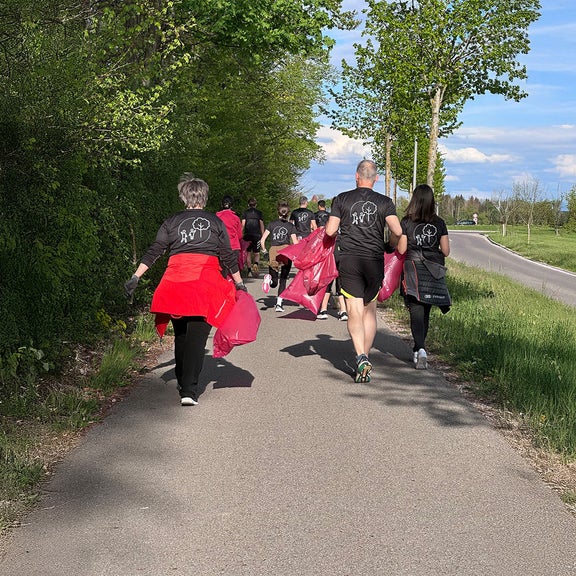 Menschen laufen auf einem Weg mit rosa Müllsäcken während einer Müllsammelaktion in einer grünen ländlichen Gegend.