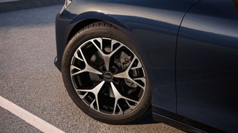 Nahaufnahme des Vorderrads eines dunkelblauen Audi mit Alufelge auf asphaltierter Straße.