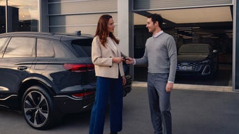A man handing a key to a woman in front of 2 Audi cars