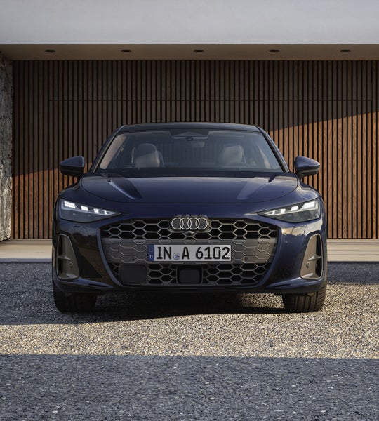 Die A6 Limousine steht im Frontprofil vor einem modernen Haus mit Holzvertäfelung.