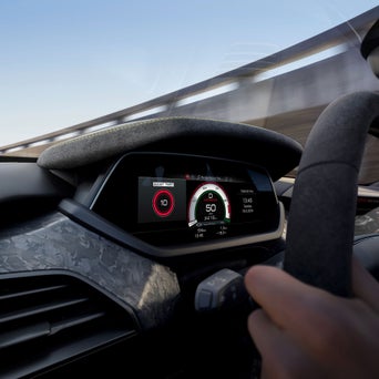 A close-up of a car's dashboard displaying speed, boost timer, and various metrics with a driver’s hand on the steering wheel.