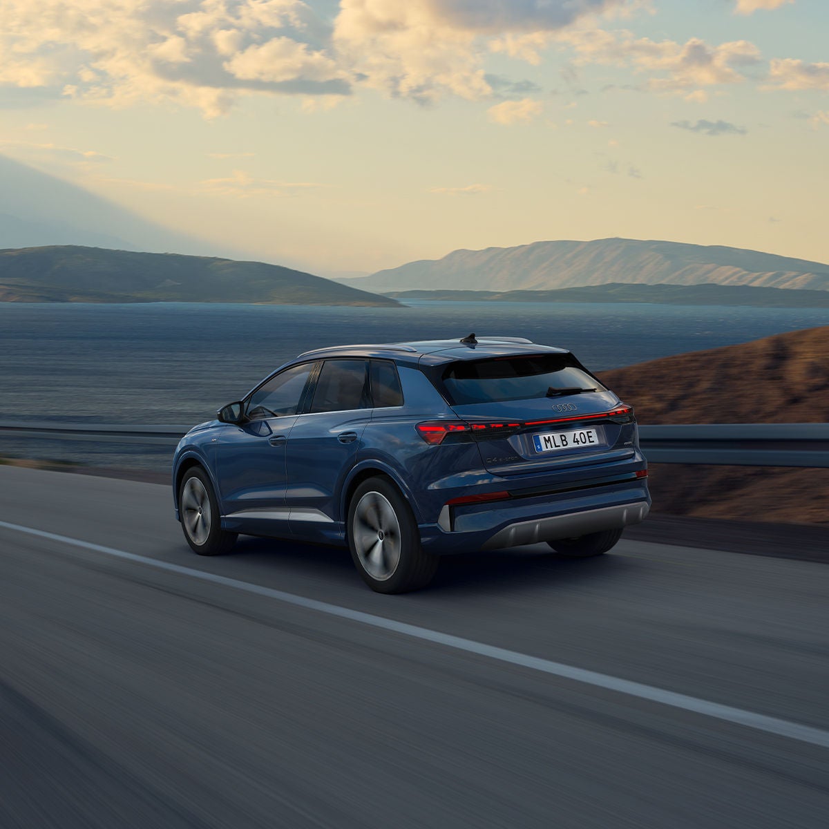 Q4 e-tron SUV sedd bakifrån på en slingrande bergsväg under natten, med havet till höger. I det mötande körfältet syns strålkastarna från fordon som närmar sig.