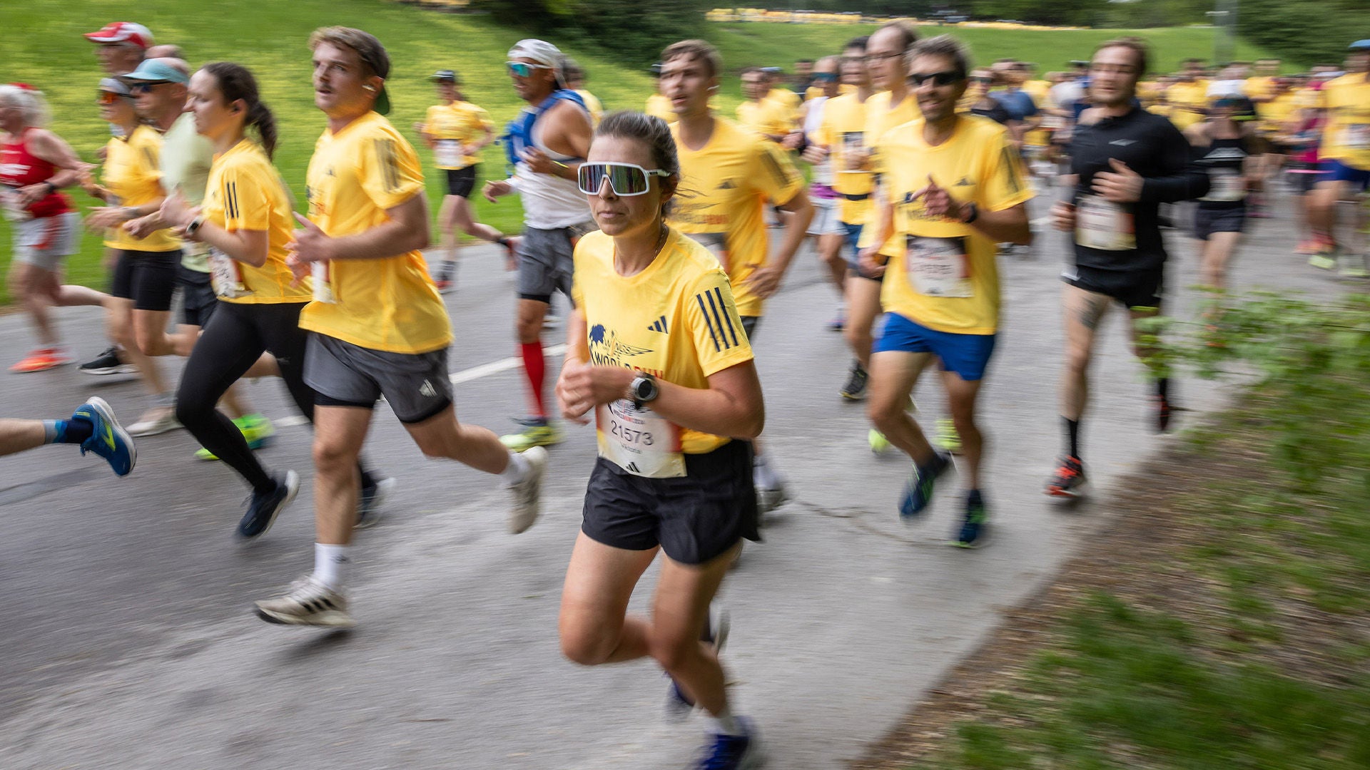 Läuferin mit weißer Sportbrille im gelben Shirt auf einer Straße, umgeben von vielen Laufenden.