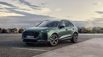 Un SUV Audi Q3 en vert métallisé est garé devant un paysage côtier sous un ciel nuageux.