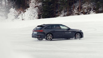 Dunkler Audi S5 Avant mit weißem Schriftzug „Audi driving experience“ driftet über schneebedeckte Fläche.