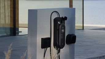 Eine Ladestation mit Kabel ist vor einem modernen Haus befestigt.