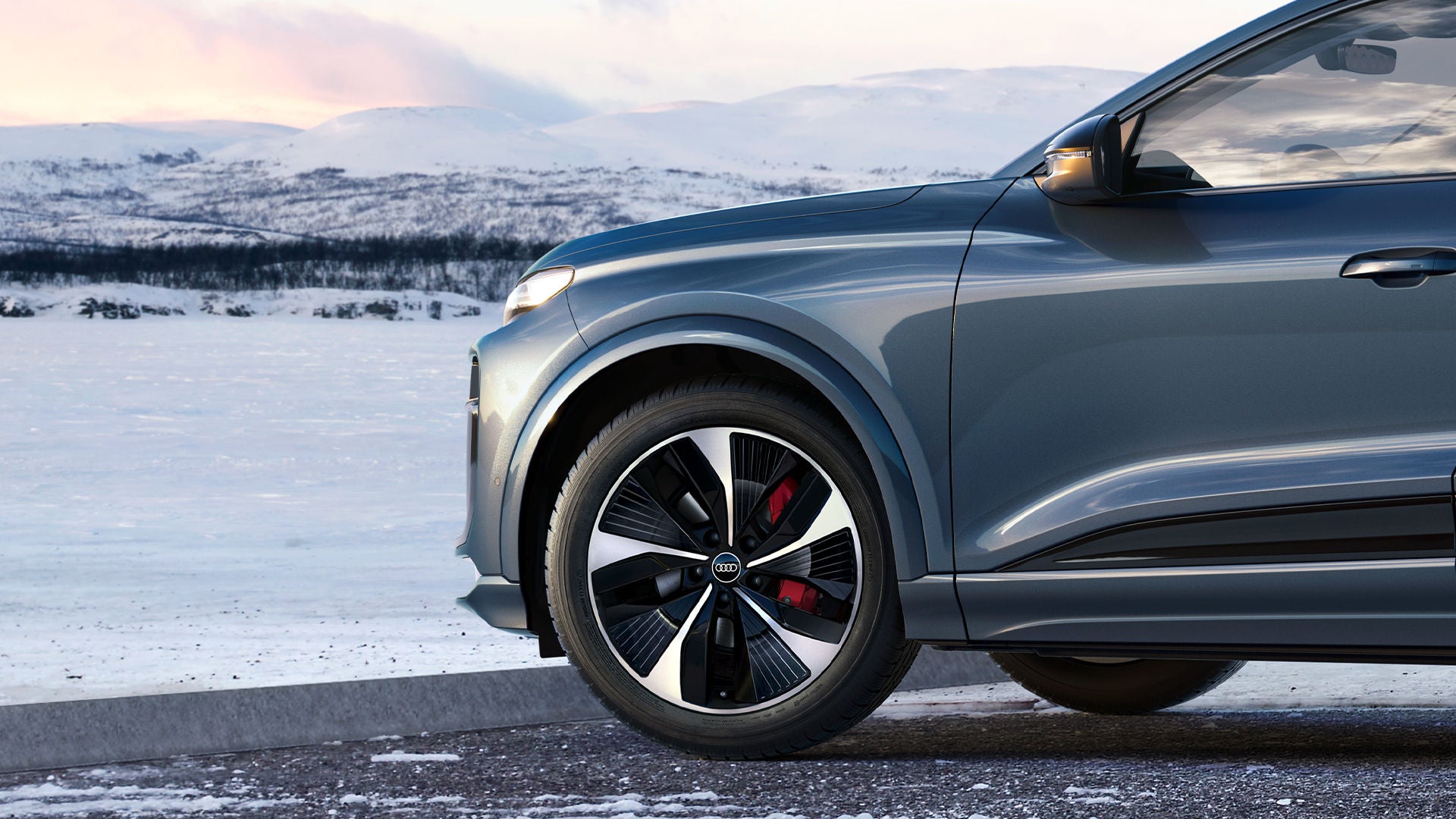 Inquadratura in primo piano delle Ruote Complete Invernali Audi, con un paesaggio innevato di montagna sullo sfondo.