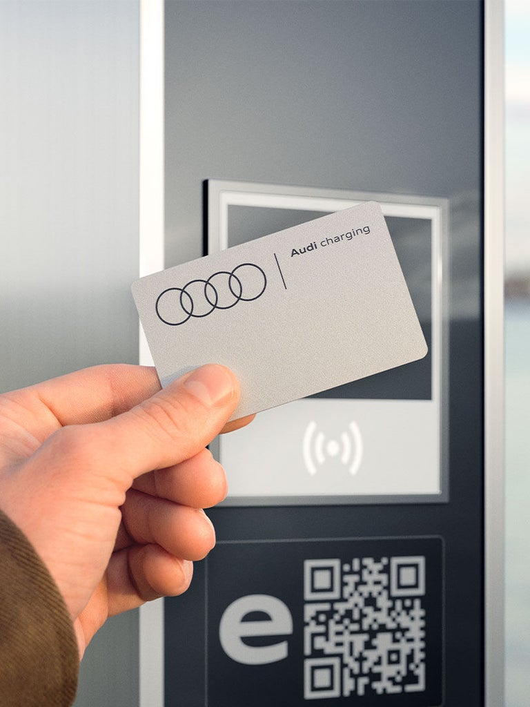 Hand hält eine Audi charging Karte vor ein Lesegerät an einer Ladesäule.
