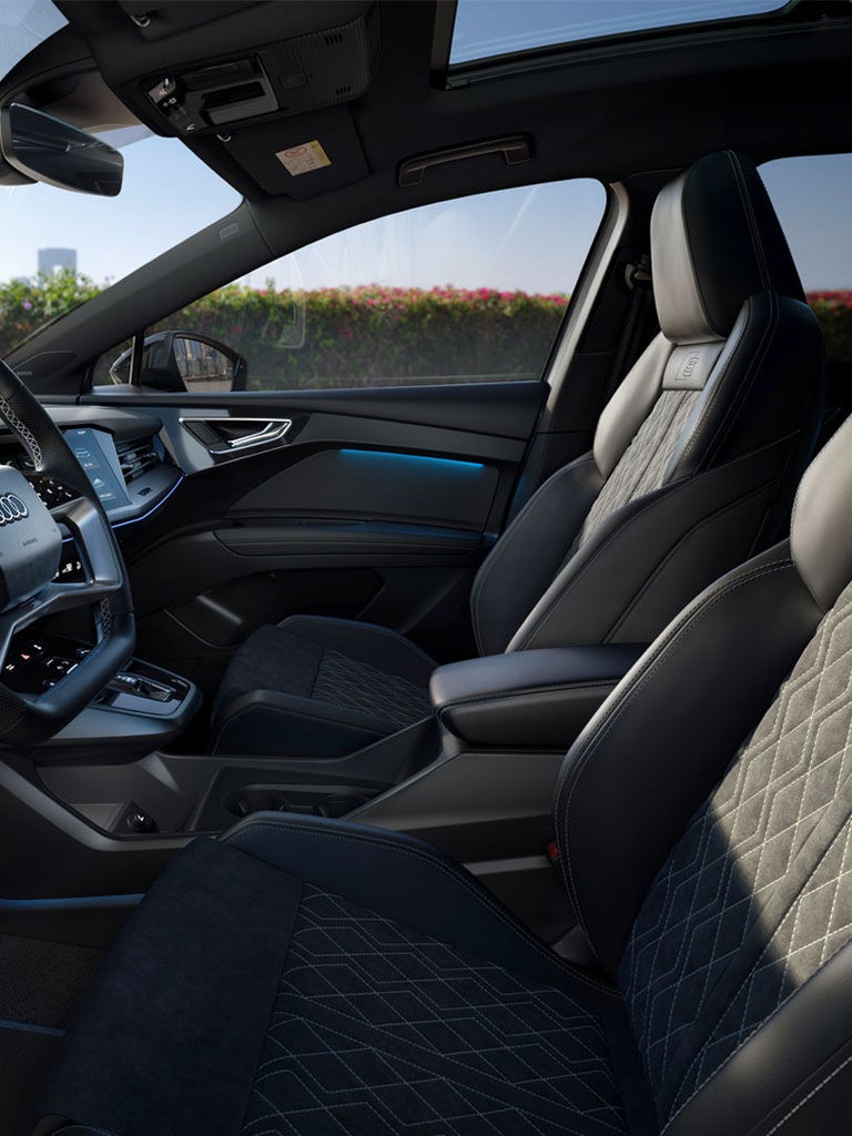 Cockpitansicht eines Audi Q4 e-tron mit Digitalanzeigen und gesteppten Sitzen, im Hintergrund Skyline mit Blumenhecke.
