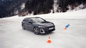 Dunkler Audi S5 Avant mit „Audi driving experience“-Schriftzug auf vereister Strecke, umgeben von Hütchen und verschneiter Waldkulisse.
