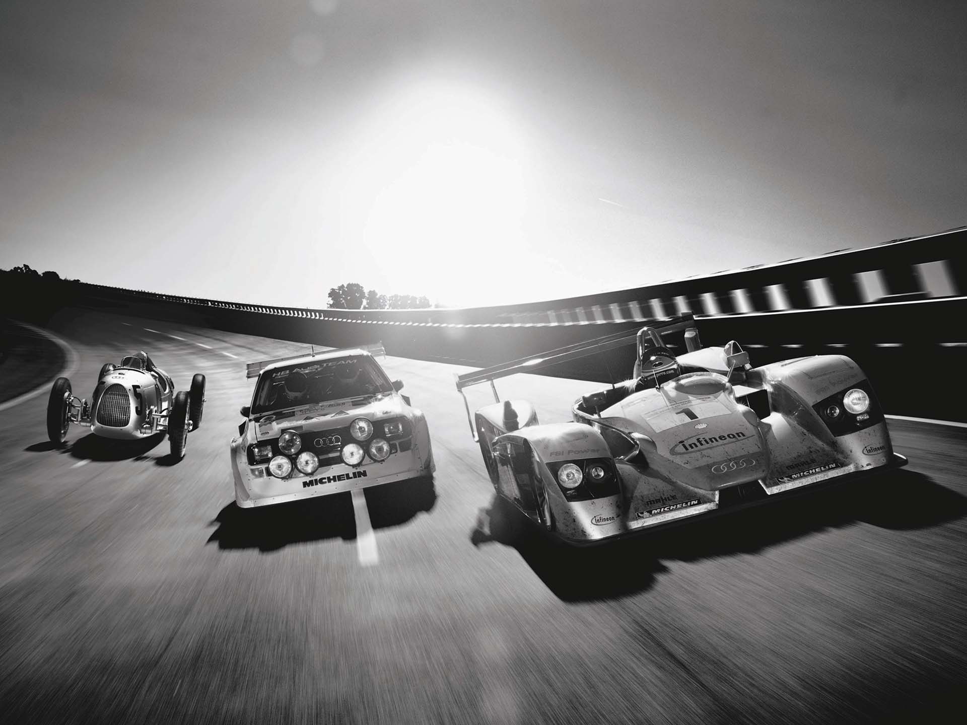 A picture showing three historic Audi race cars side by side on a banked racetrack.