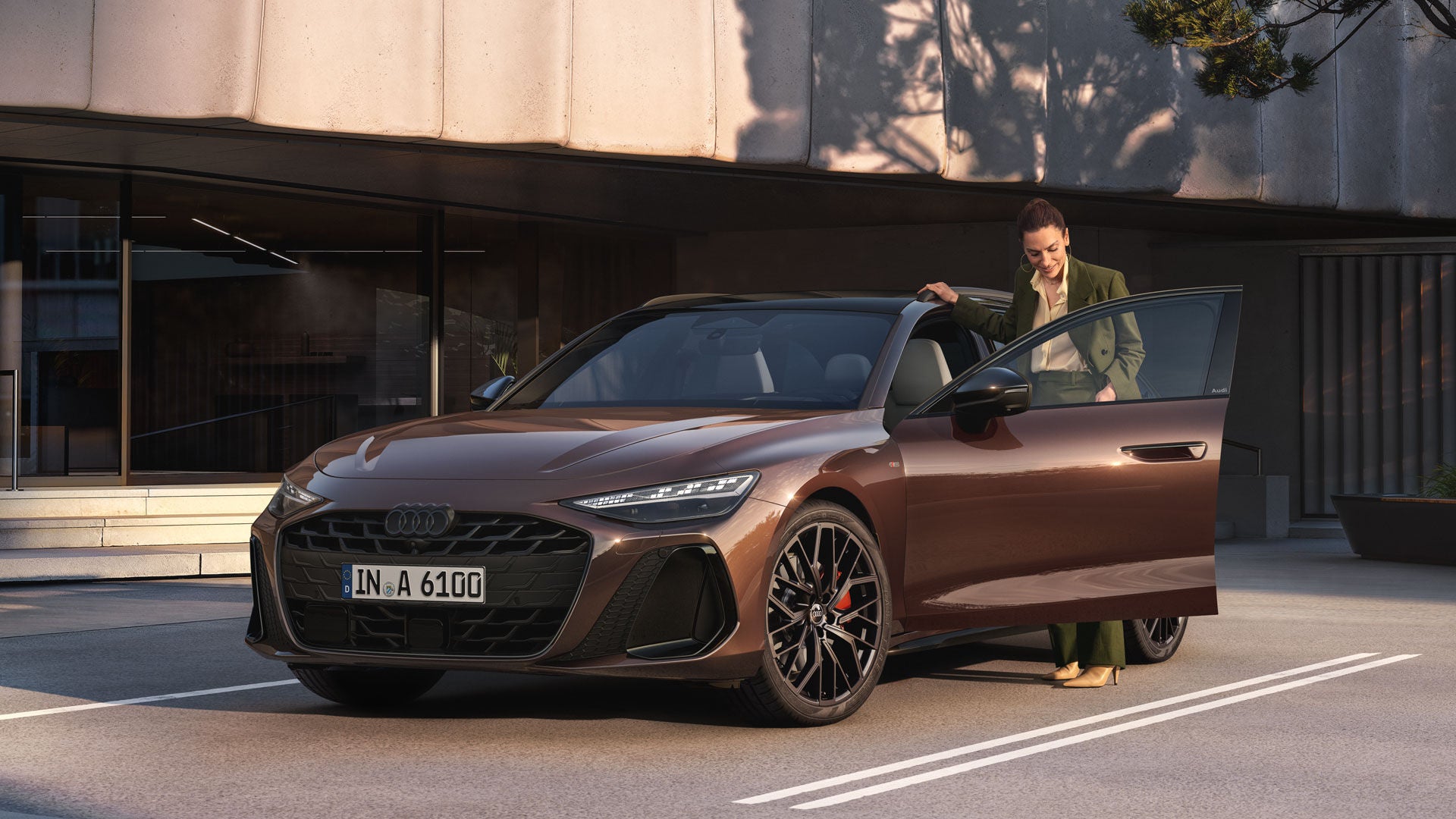 Frau steigt bei Sonnenuntergang vor modernem Gebäude in einen braunen Audi A6 mit geöffnetem Fahrerinnentür ein.