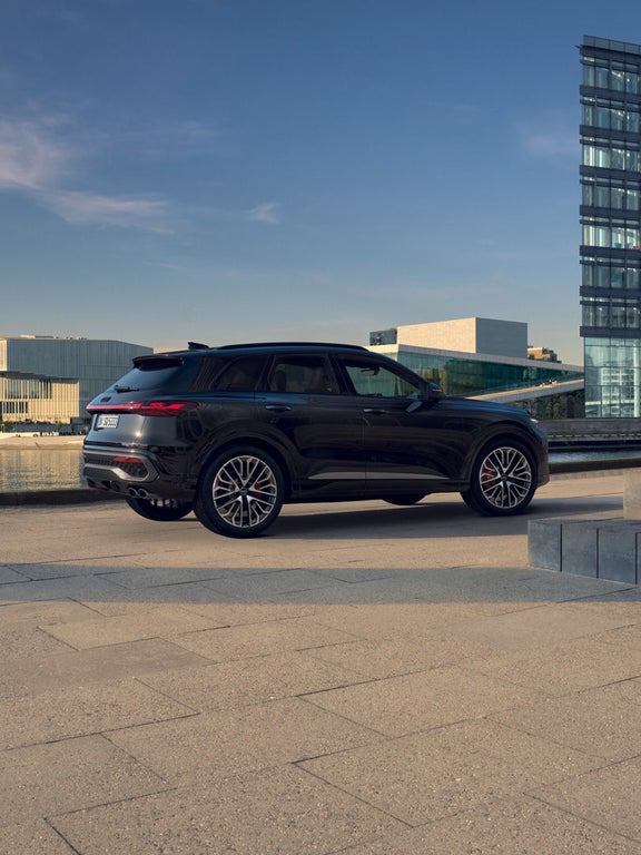 Ein schwarzer Audi SQ5 SUV von hinten seitlich, vor moderner Architektur am Wasser geparkt.