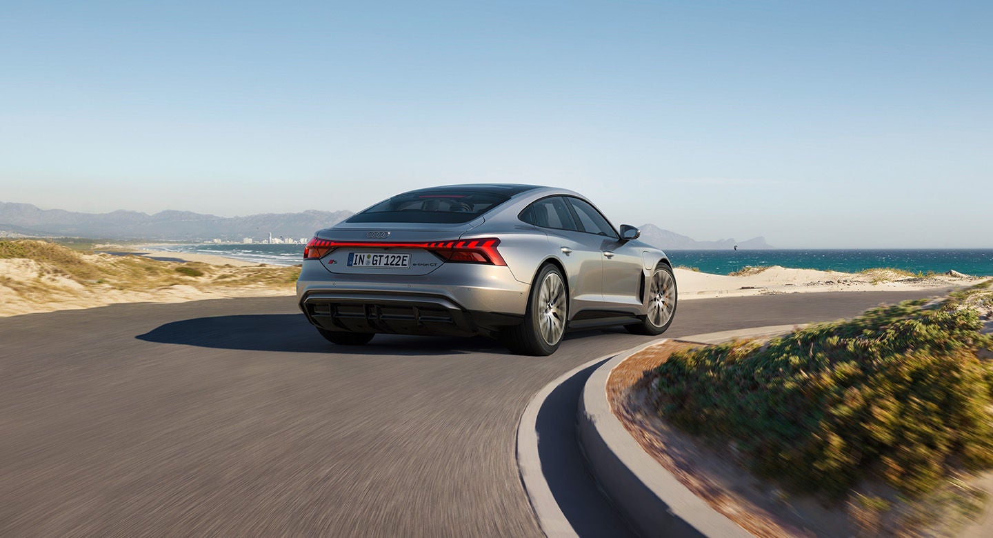 A silver Audi S-e-tron GT driving along a coastal road with mountains in the distance.