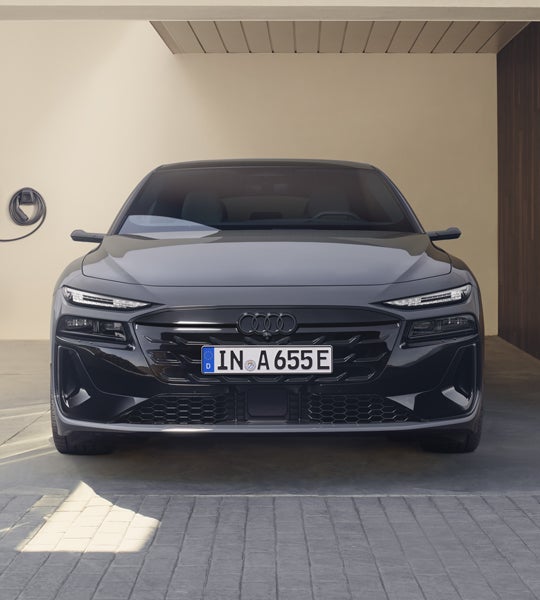 Frontprofil des A6 Avant e-tron, welcher vor einer weißen Hausfassade steht.