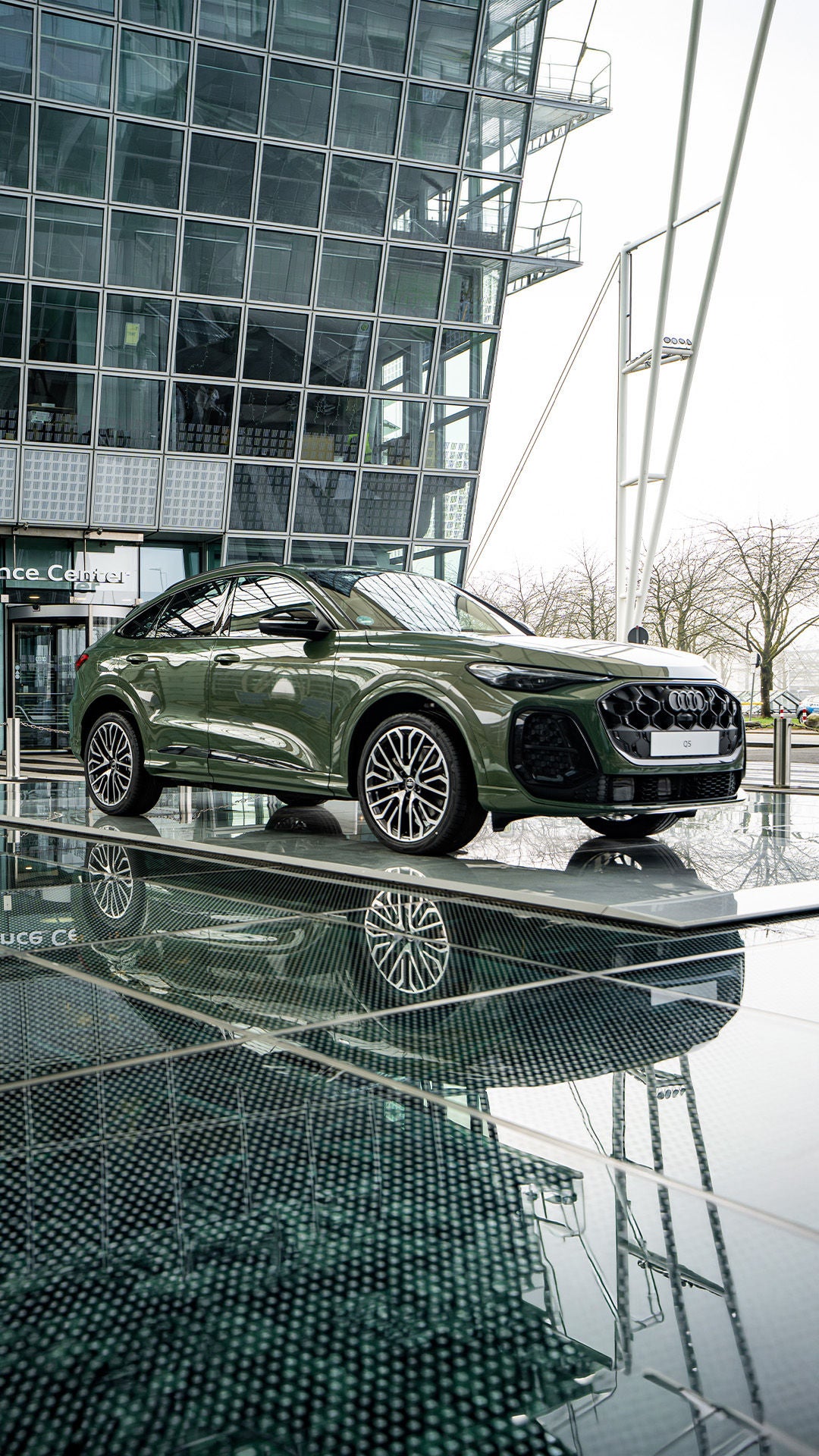 Grüner Audi Q5 steht vor dem Audi Conference Center, Glasfassade und Spiegelung im Vordergrund sichtbar.