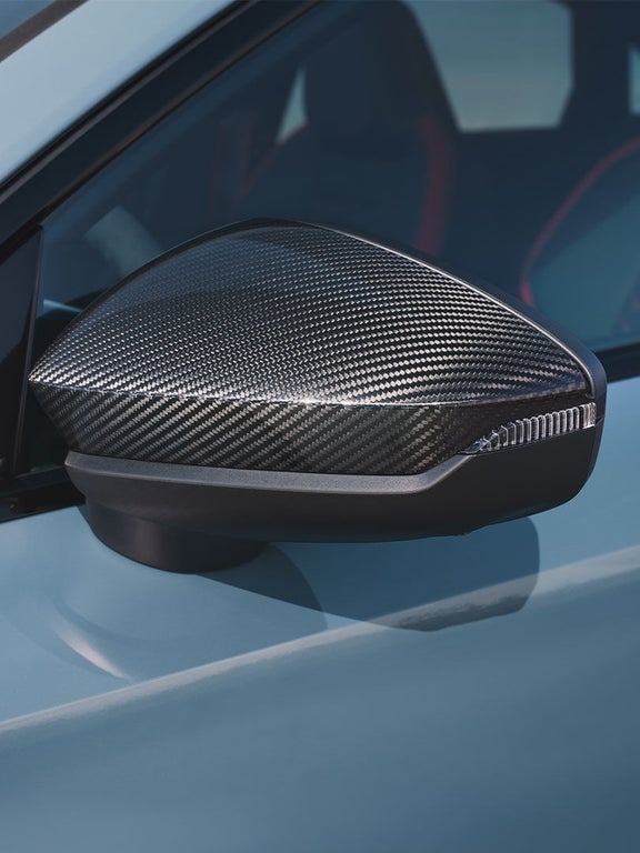 Nahaufnahme eines Außenspiegels mit glänzender Carbonfaser-Oberfläche an einer hellblauen Audi RS 3 Limousine.