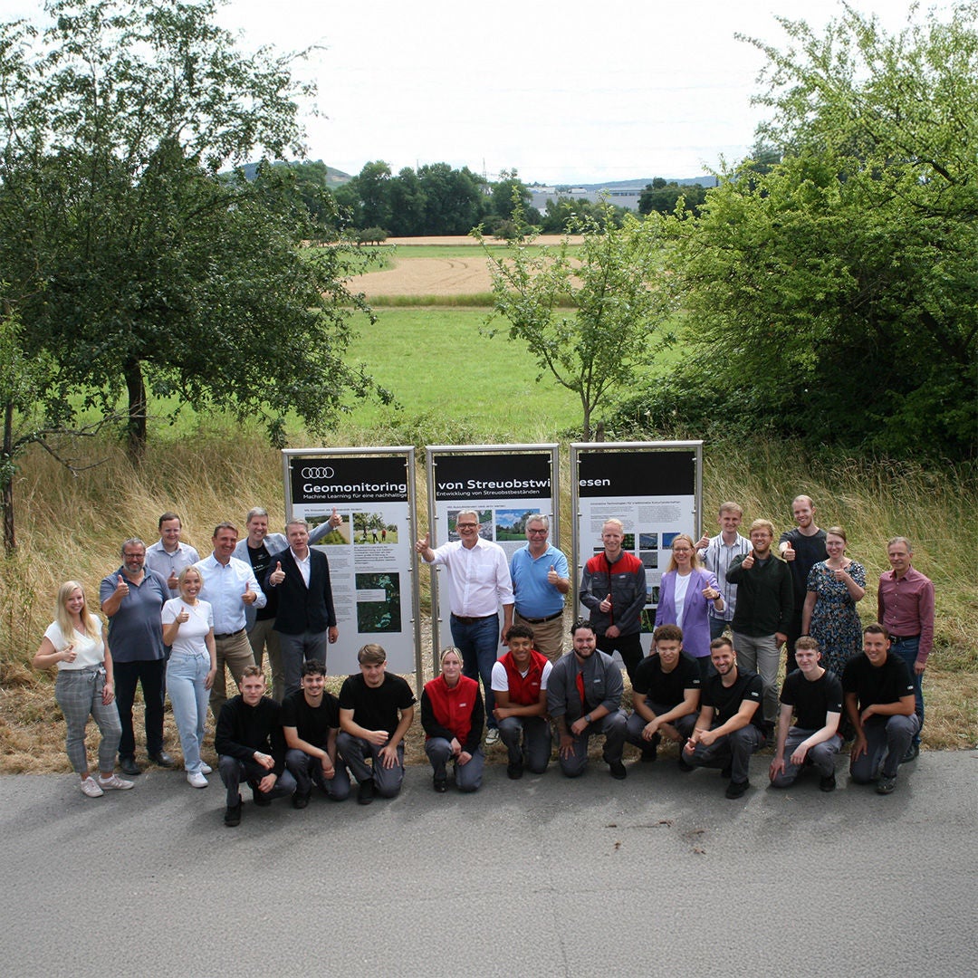 Group photo in front of information boards on geomonitoring and orchard meadows, taken in a rural setting.