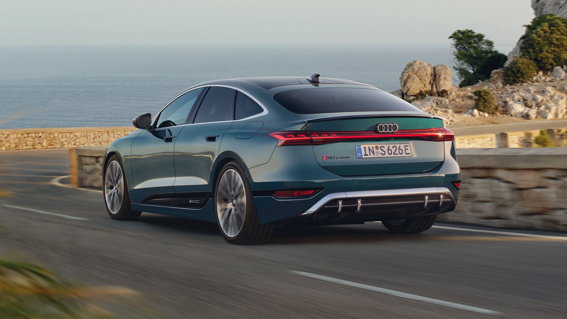 Der S6 Sportback e-tron im schrägen Heckprofil, während er eine kurvige Küstenstraße entlangfährt.