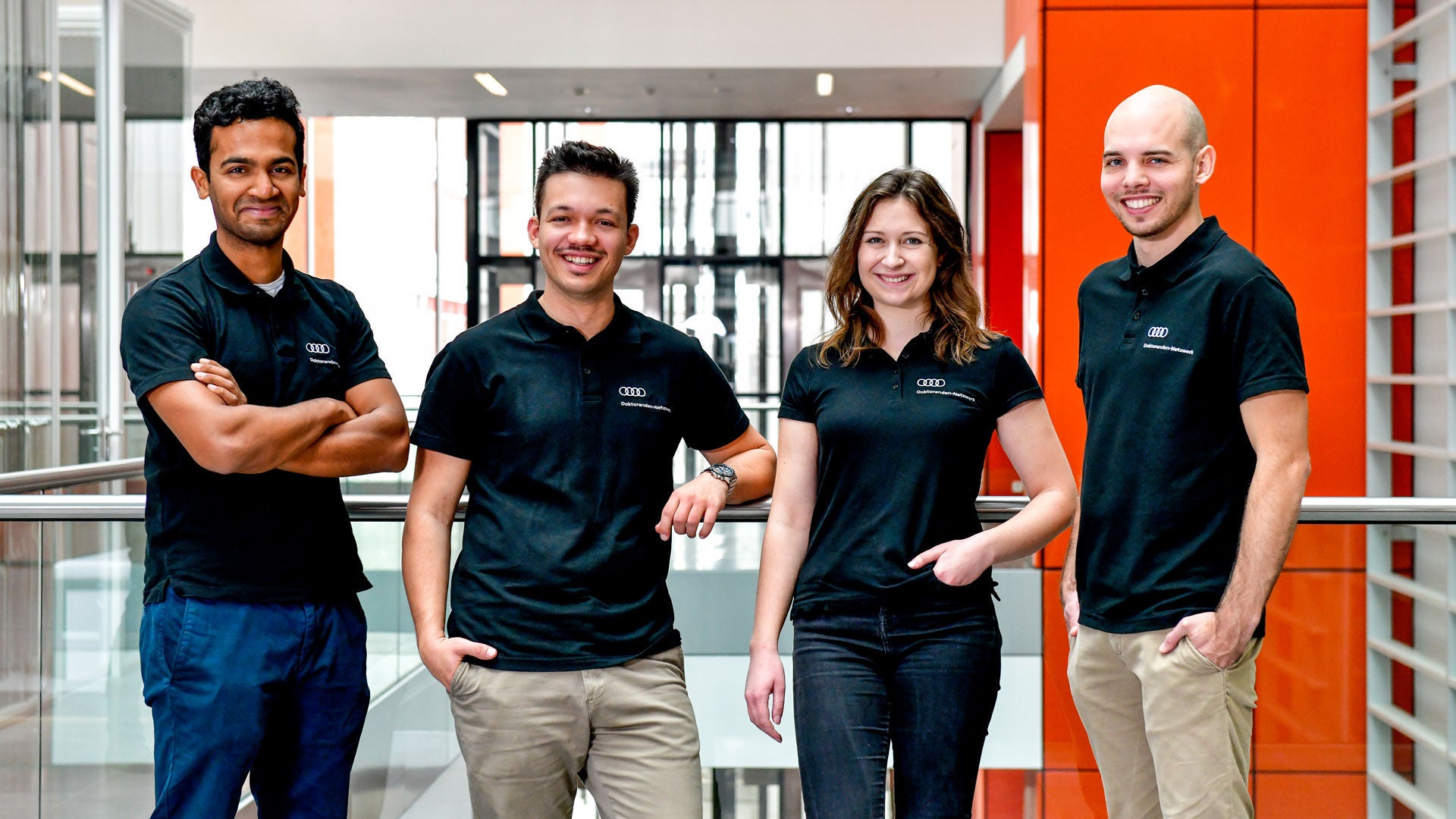 Vier Absolventen in AUDI Shirt stehen nebeneinander in einem Gang