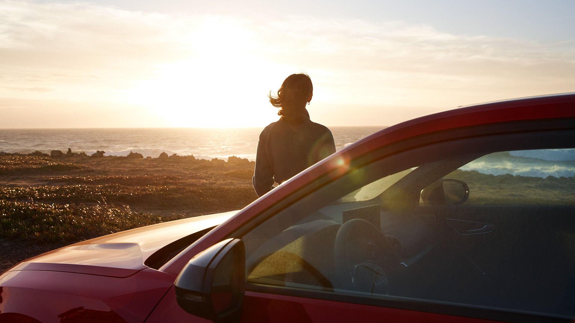 Person leaning on a car watching the sunset over the ocean.