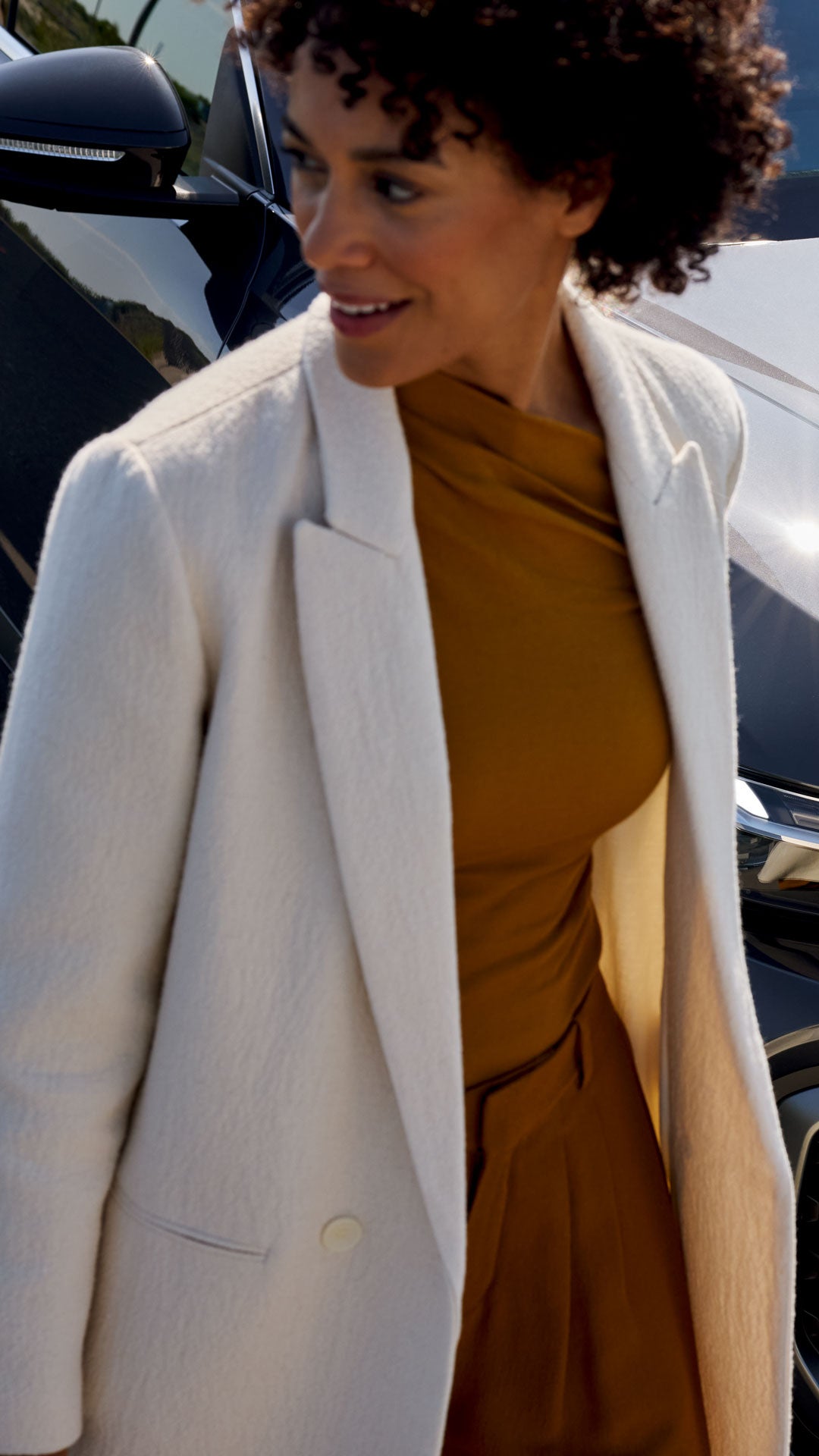 Frau in beiger Jacke steht neben einem blauen Audi Q5, aufgenommen von schräg oben, mit Fokus auf Fahrzeugfront und Kühlergrill.