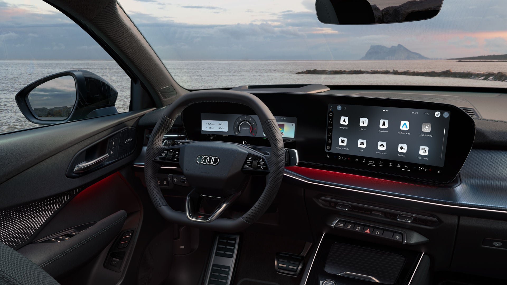 Rear view of the cockpit of the Q3 Sportback with steering wheel, panoramic display, and red ambient lighting package. The sea can be seen through the windshield.