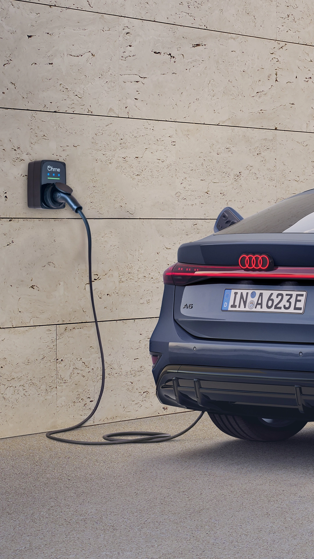 A grey Audi parked and charging at a wall-mounted electric charger next to a modern stone wall.