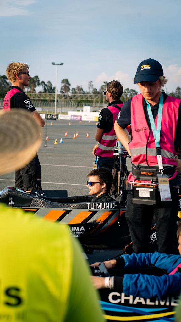 Ein paar Personen stehen auf einem Übungsplatz, während zwei Personen in Rennautos sitzen