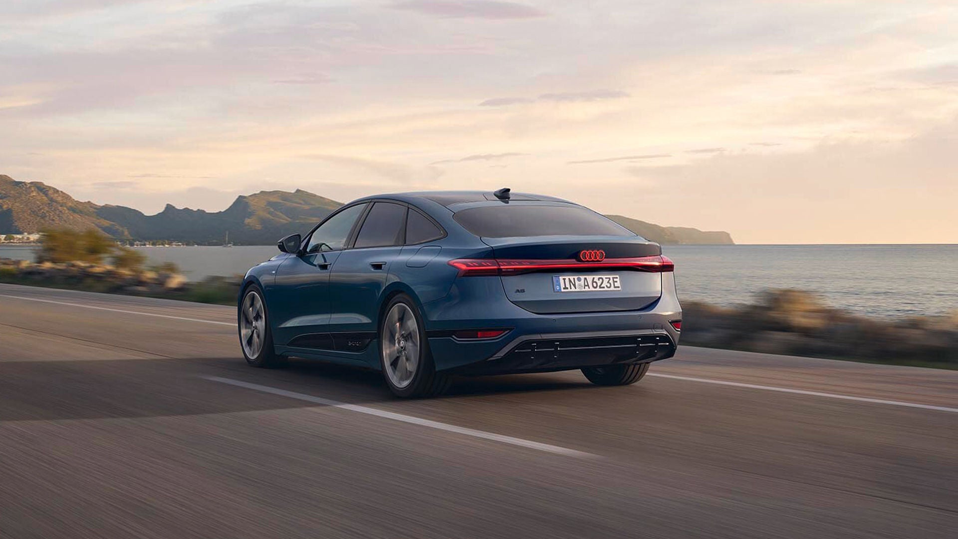Blauer Audi A6 Sportback e-tron fährt auf Straße am Meer, Heckansicht