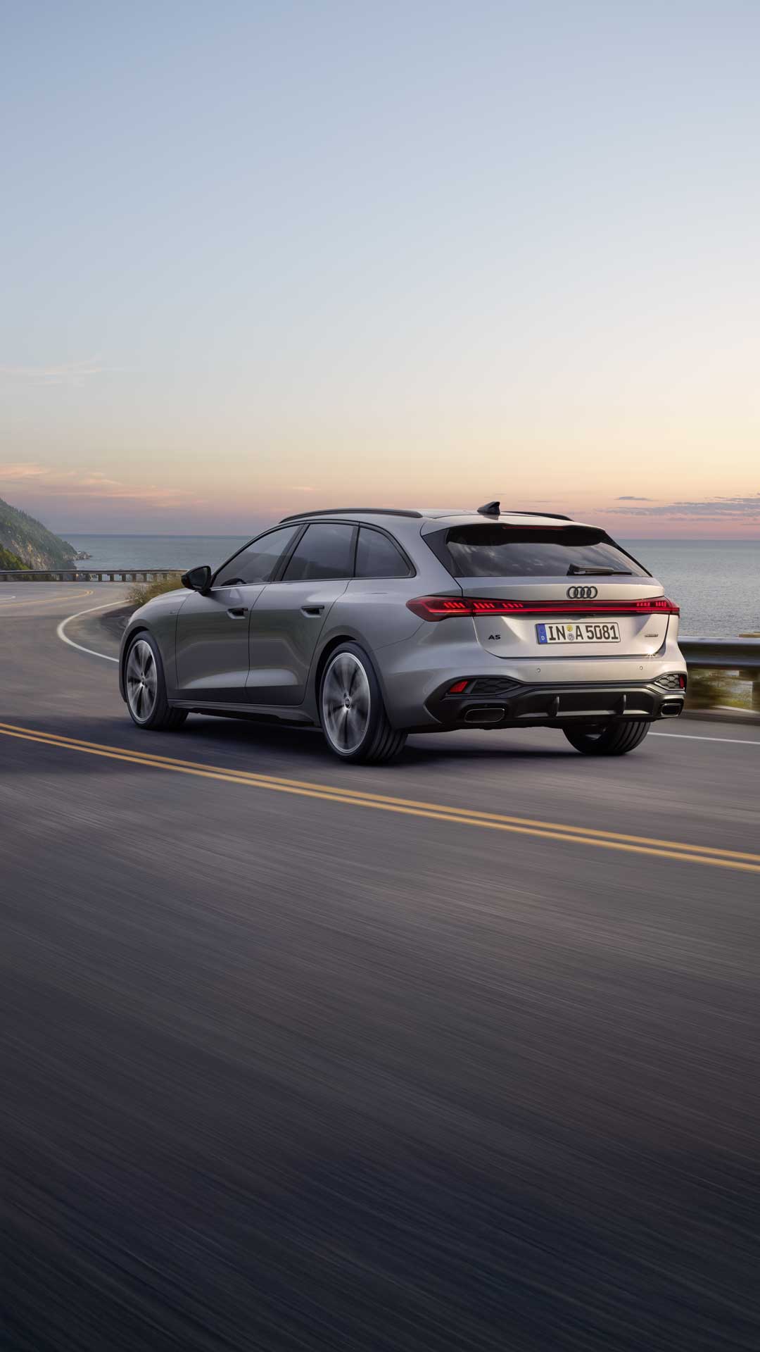Der A5 Avant in einer schrägen Heckperspektive, während er bei Sonnenuntergang eine kurvige Küstenstraße entlangfährt.