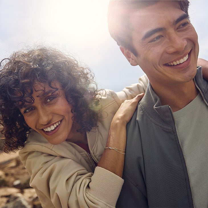 Un couple souriant se tenant par l'épaule en plein air sous un soleil éclatant.