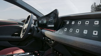 Innenraum-Aufnahme eines Audi-Cockpits seitlich durch die Fahrertür. Im Fokus steht das Beifahrerdisplay. Im Hintergrund sind Mittelkonsole, Lenkrad und weitere Displays zu erkennen. 