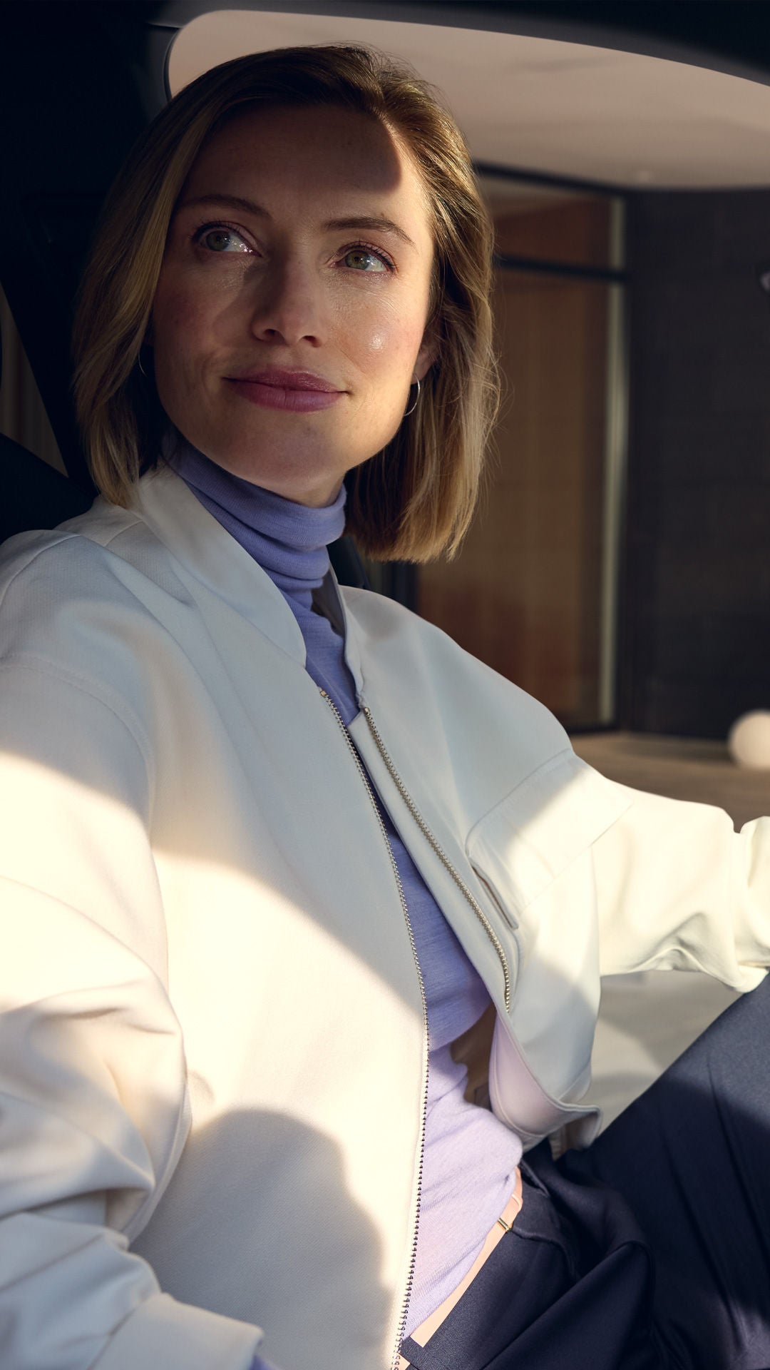 Eine Frau sitzt im Innenraum eines Audi und hat eine Hand am Lendrad. Die Fahrertür steht offen und die Frau guckt schräg nach hintern.