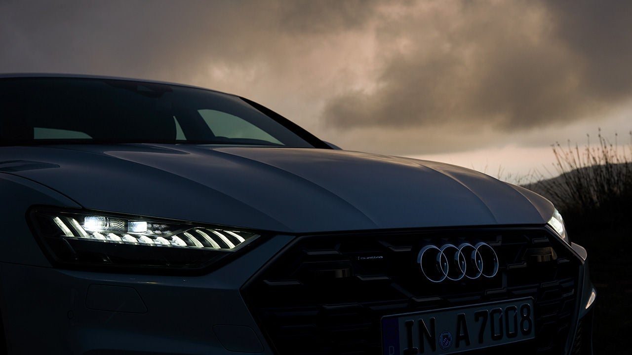 Frontansicht eines Audi bei Dämmerung mit eingeschaltetem LED-Tagfahrlicht, dunkle Wolken im Hintergrund.