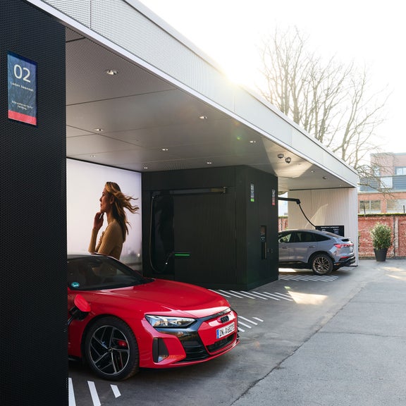 Zwei Audi Elektroautos laden an modernen Ladesäulen auf einem urbanen Parkplatz.