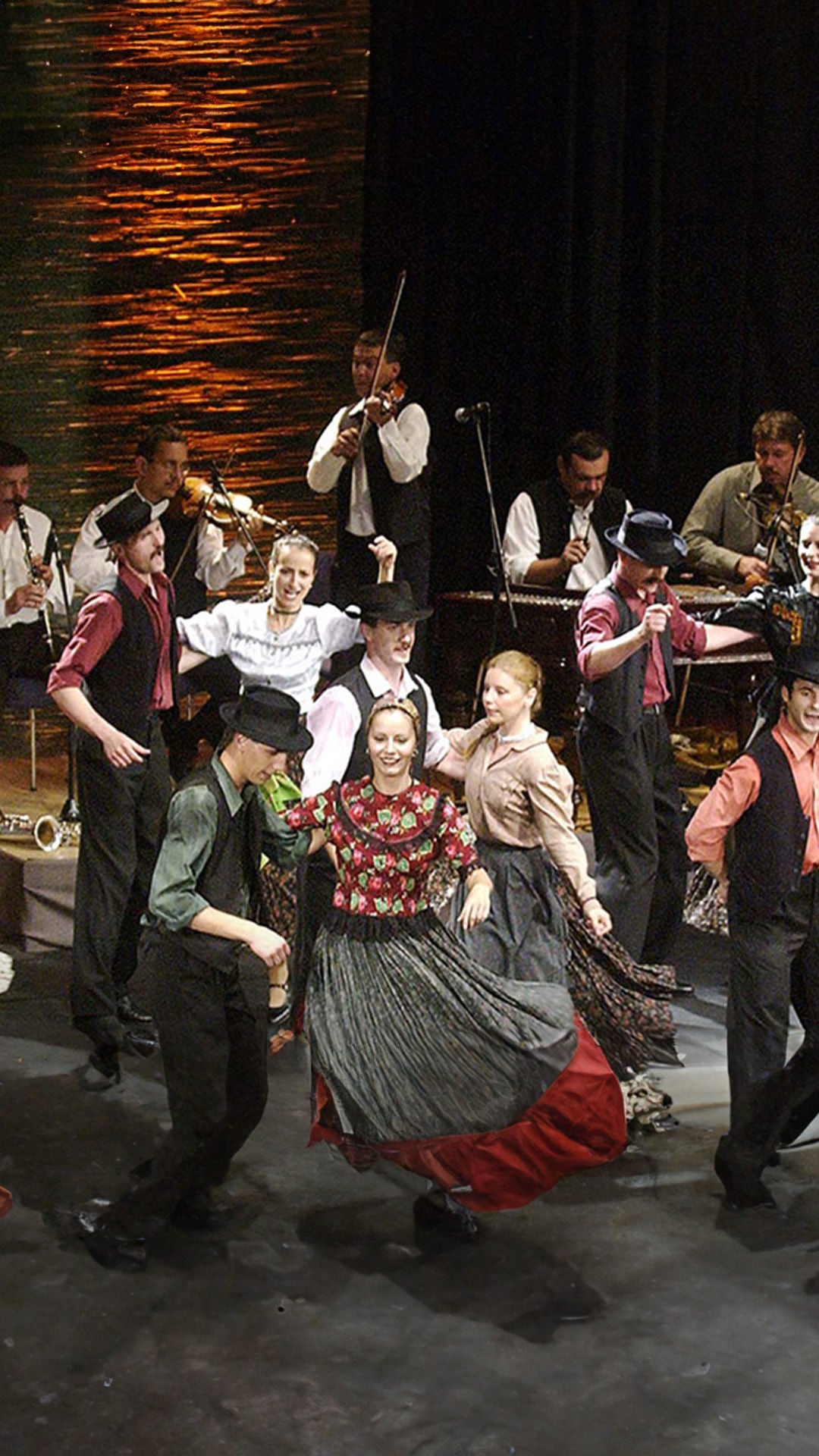 Eine Gruppe kostümierter Menschen tanzen auf einer Bühne.