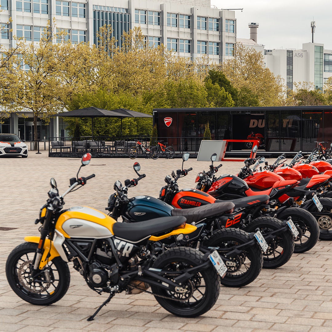 Mehrere Ducati-Motorräder stehen in Reihe auf Platz vor modernem Gebäude.