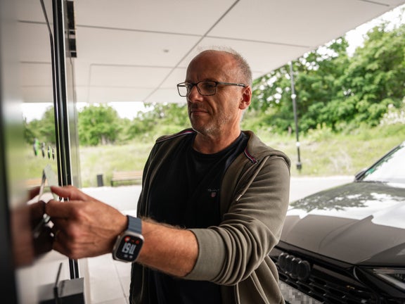 A man holds a card to the NFC surface of the Audi charging hub