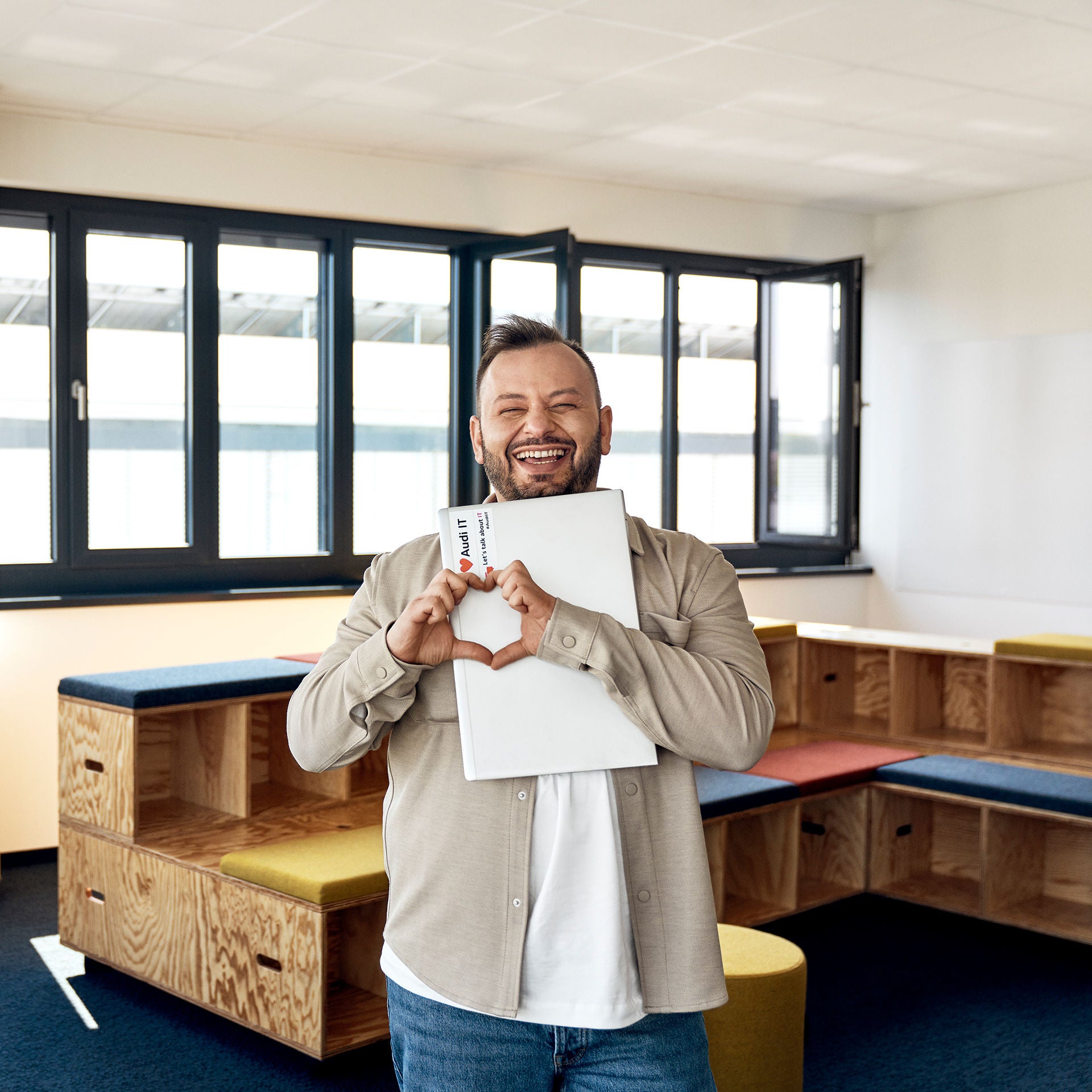 Buenyamin shows a heart with his hands and has his laptop clutched in his arms. He laughs into the camera