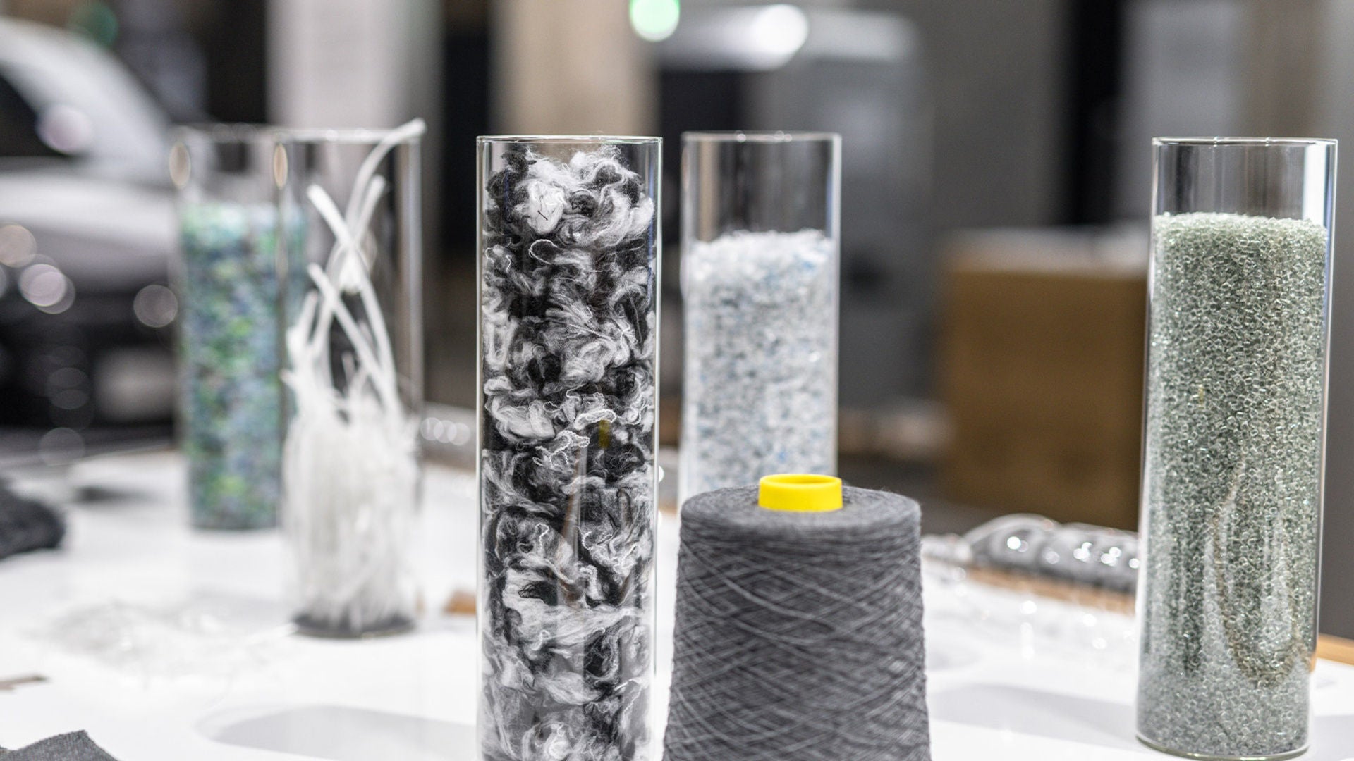 Several glass cylinders containing fibers and granules and a gray spool of thread on a table